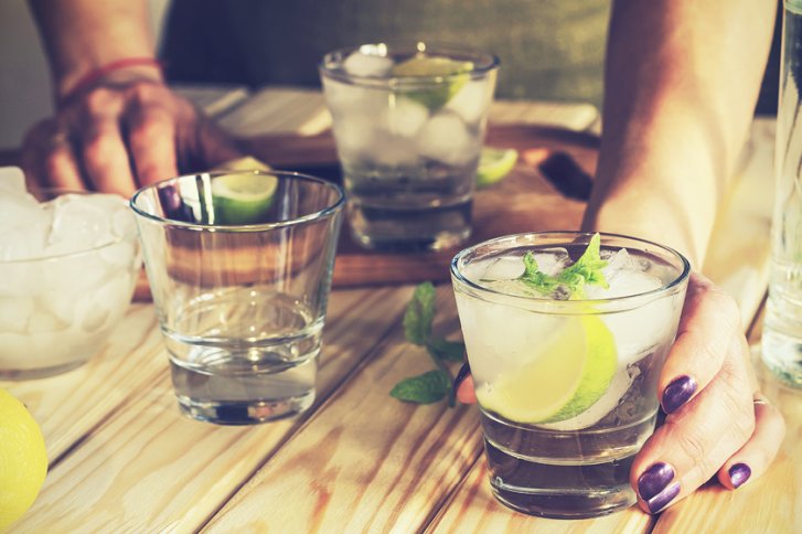 Getränkeglas - wird gehalten - auf einem Holztisch mit Limetten und Eis.