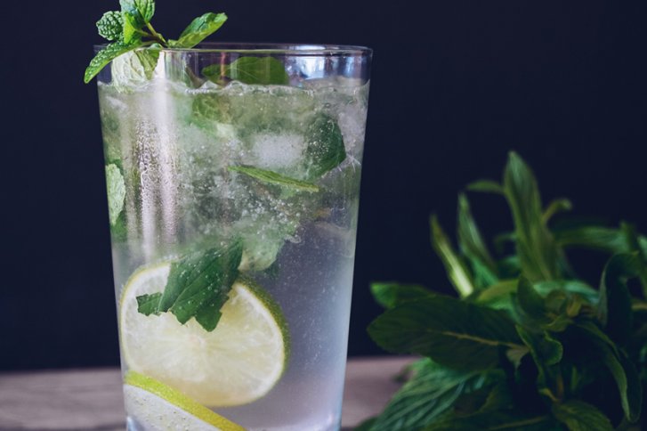 Ein Glas mit Mojito, gefüllt mit Eis und Limettenscheiben, steht auf einem Holztisch.
