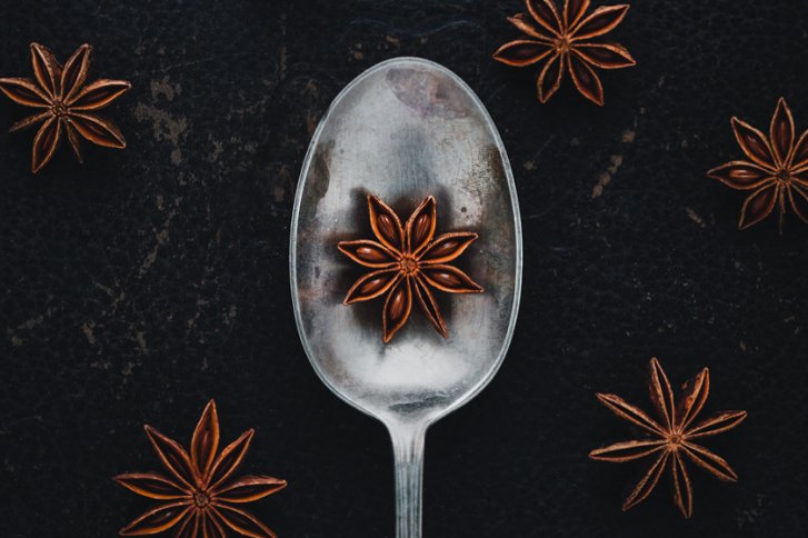 Löffel - hält Anis - auf dunklem Untergrund mit weiteren Anissternen verstreut.