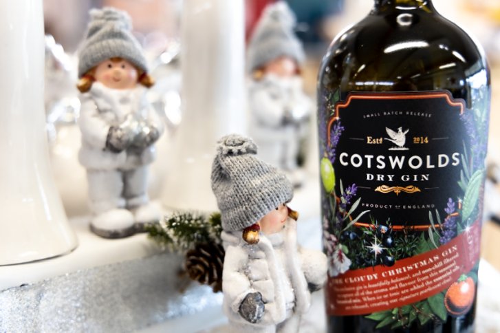 Flasche Cotswolds Dry Gin neben kleinen winterlichen Figuren in gemütlicher, festlicher Dekoration.