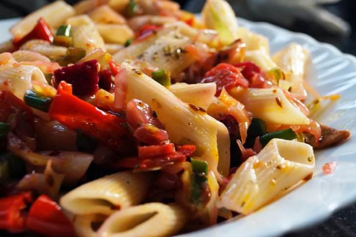 Nudeln, gemischt mit buntem Gemüse, liegen dekorativ auf einem weißen Teller in einer Küche.