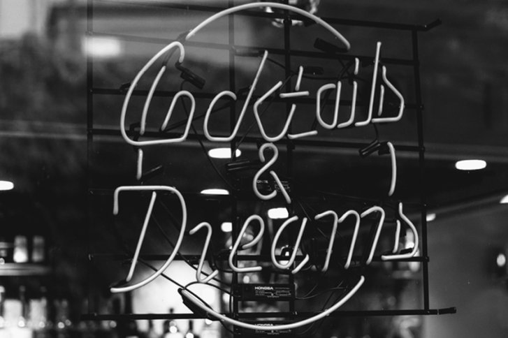 Leuchtreklame zeigt "Cocktails & Dreams", hängt vor einer Bar mit unscharfem Hintergrund.