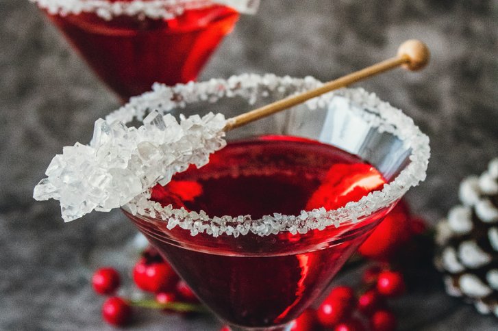 Roter Cocktail in Glas mit Zuckerrand, dekoriert mit Zuckerstick, auf dunklem Hintergrund.