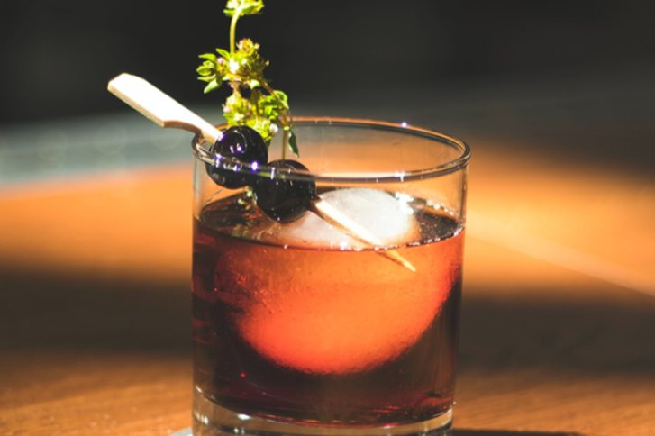 Ein Cocktailglas steht auf einem Tisch, gefüllt mit Getränk, Eiswürfel und Dekoration.