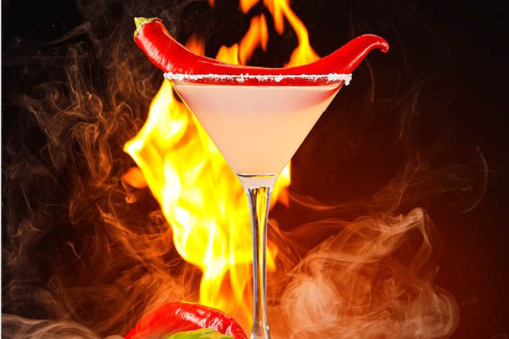 Cocktailglas mit Chili oben, umgeben von Feuer und Rauch im dramatischen Hintergrund.