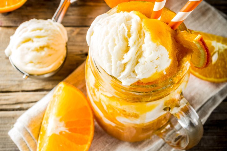 Creamsicle im Glas mit Orangenhälfte und Kugel Eis auf hellem Hintergrund.