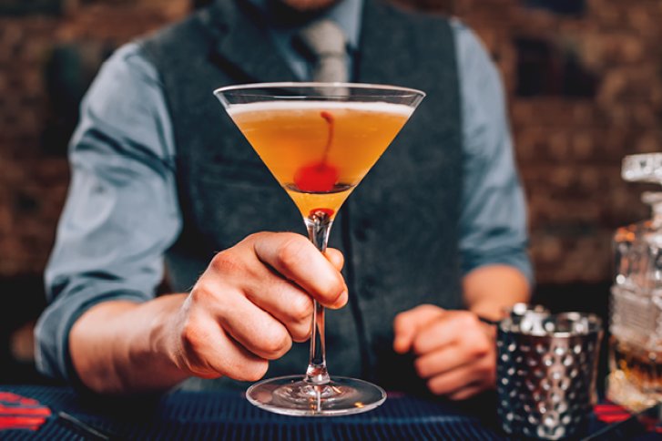 Ein Mann hält ein Cocktailglas mit Kirsche in einer Bar.