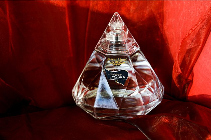 Kristallflasche steht auf rotem Stoffuntergrund, Etikett mit "Jewel Lines" und "Vodka" sichtbar.