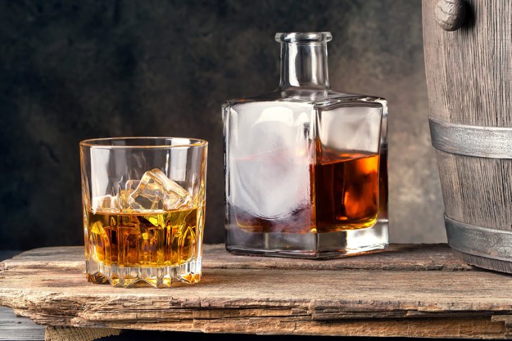 Glas mit Eiswürfeln, gefüllt mit Whiskey, steht neben einer Karaffe auf rustikalem Holztisch.