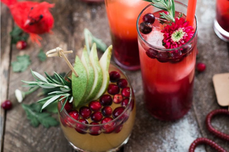 Cocktails stehen dekoriert mit Beeren und Kräutern auf einem rustikalen Holztisch.
