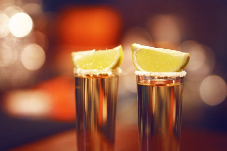 Zwei Tequila-Shots mit Salzrand und Limettenscheiben stehen auf einem Tisch in gedämpfter Beleuchtung.
