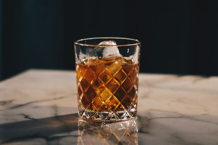 Ein Kristallglas mit Getränk und Eiswürfeln steht auf einem eleganten Marmortisch.