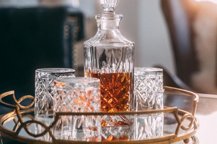 Kristallkaraffe mit brauner Flüssigkeit und Gläsern auf verziertem Tablett in elegantem Raum.