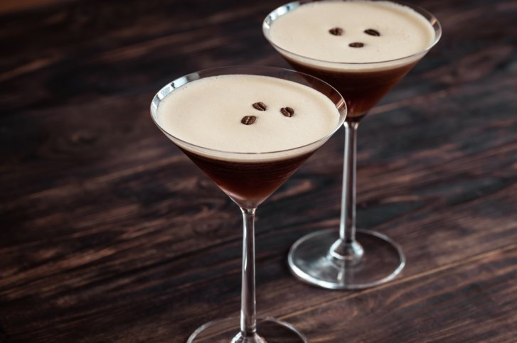 Zwei Martinigläser mit Espresso-Martinis stehen auf einem dunklen Holztisch.