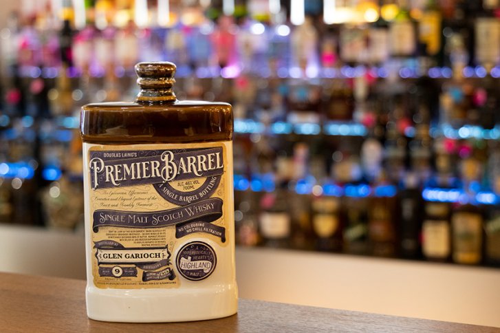 Eine Whiskykaraffe steht auf einer Theke vor einem verschwommenen Regal mit Flaschen.