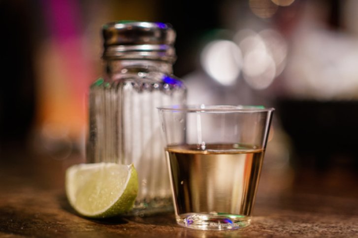 Ein Tequila-Shotglas steht vor einem Salzstreuer, daneben liegt eine Limettenscheibe.