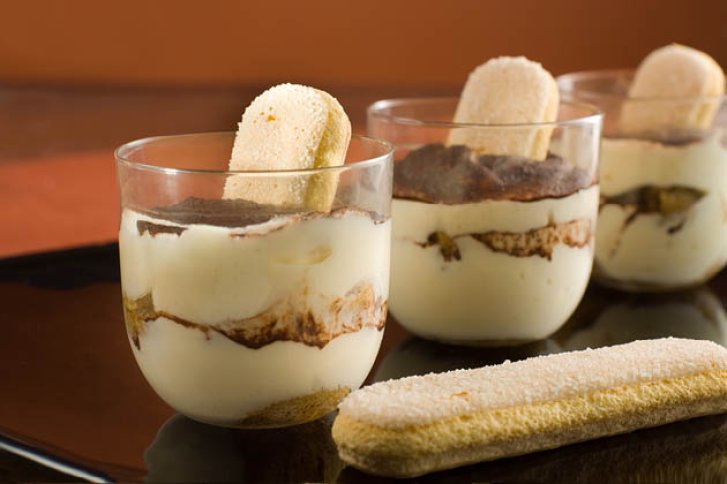 Gläser mit Tiramisu-Schichten und Löffelbiskuit stehen auf einem dunklen Tablett.