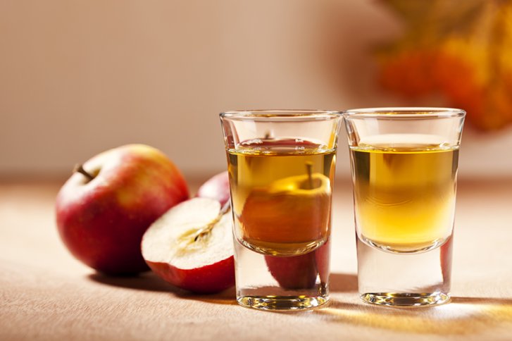 Zwei Gläser mit Apfelschnaps stehen auf Tisch, daneben liegen rote Äpfel.