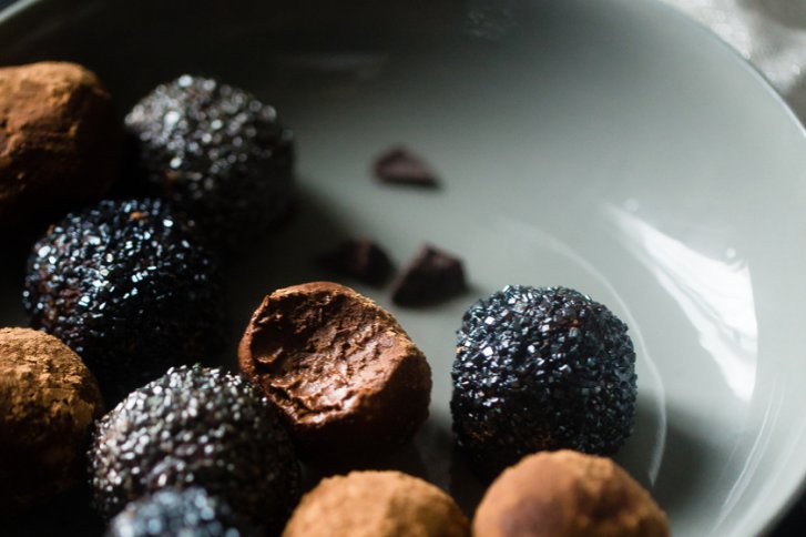 Schokoladentrüffel liegen auf einem grauen Teller, dekoriert mit dunklen Streuseln und Kakaopulver.