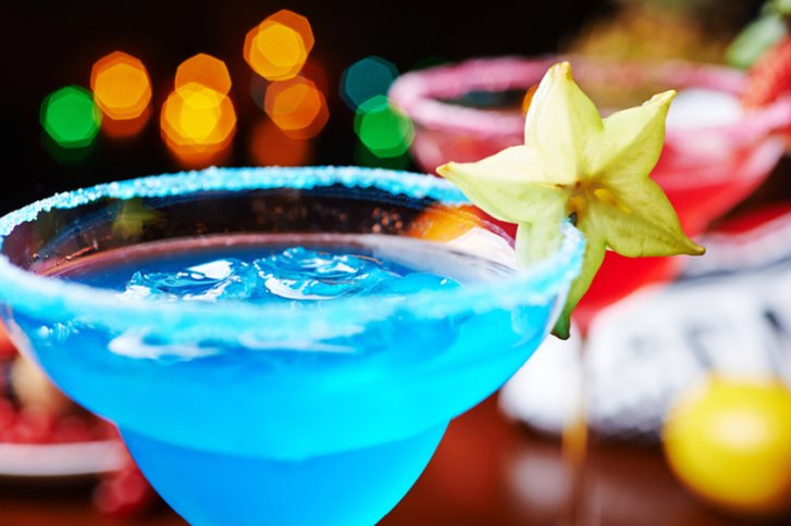 Blauer Cocktail mit Zuckerrand und Sternfruchtdeko, beleuchtet von bunten Lichtern im Hintergrund.