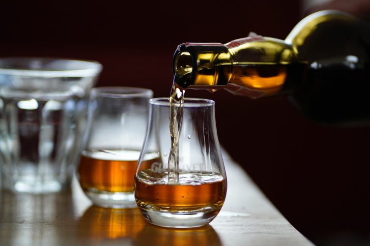 Flasche gießt Whisky in ein Glas, auf einem Holztisch mit weiteren Gläsern.