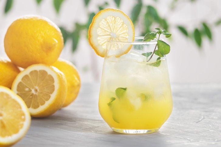 Ein Glas Zitronencocktail steht mit Eis und Minze auf einem Tisch neben frischen Zitronen.