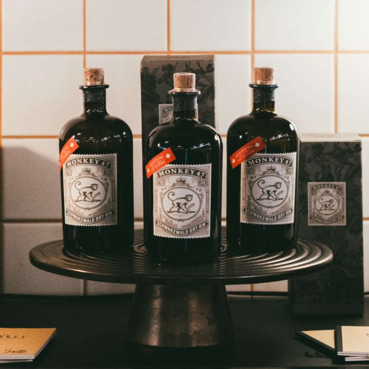 Drei Ginflaschen stehen auf einem Tablett, umgeben von Verpackungen, vor gekachelter Wand.