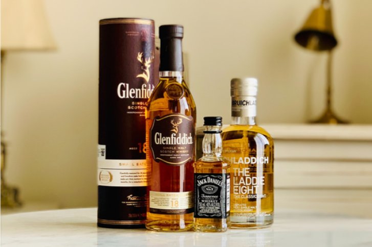 Vier Whiskyflaschen stehen nebeneinander auf einem Tisch in einem gemütlichen Raum.