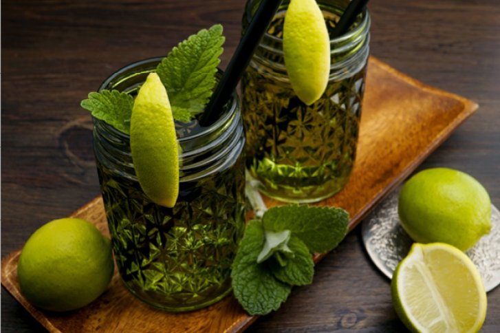 Zwei Gläser mit grünem Getränk, dekoriert mit Zitronenscheiben und Minze, auf Holztablett.