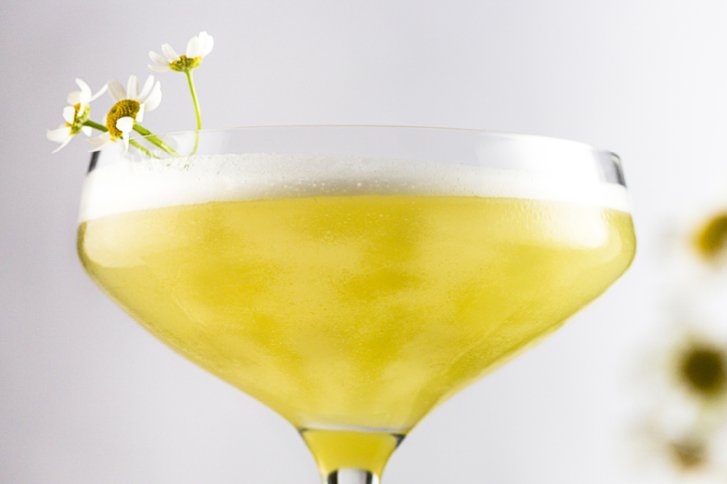 Ein mit Schaumwein gefülltes Glas, dekoriert mit kleinen weißen Blumen vor hellem Hintergrund.