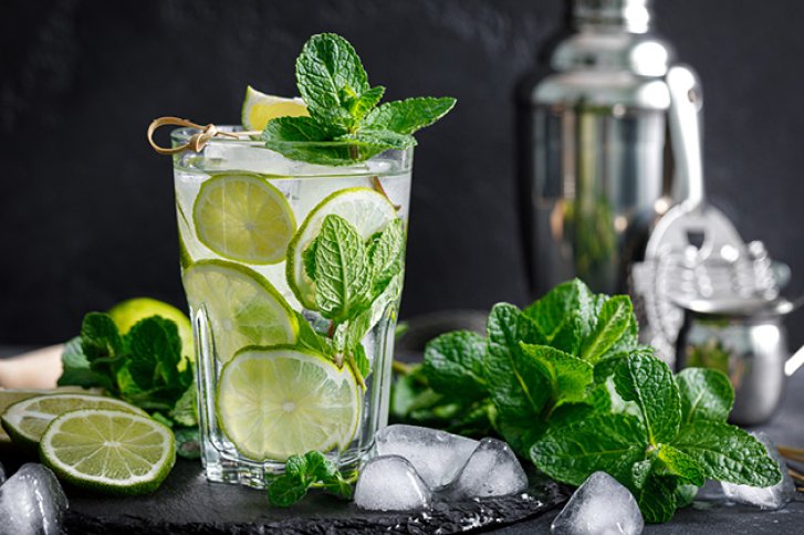 Ein Glas Mojito mit Limettenscheiben und Minze steht auf einem Tisch mit Eiswürfeln.