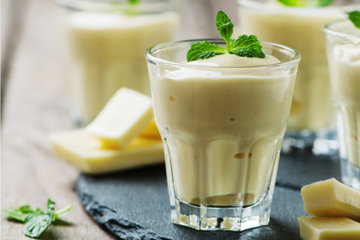 Ein Glas Weißeschokoladencreme mit Minzblättern dekoriert, steht auf einem Schieferbrett.