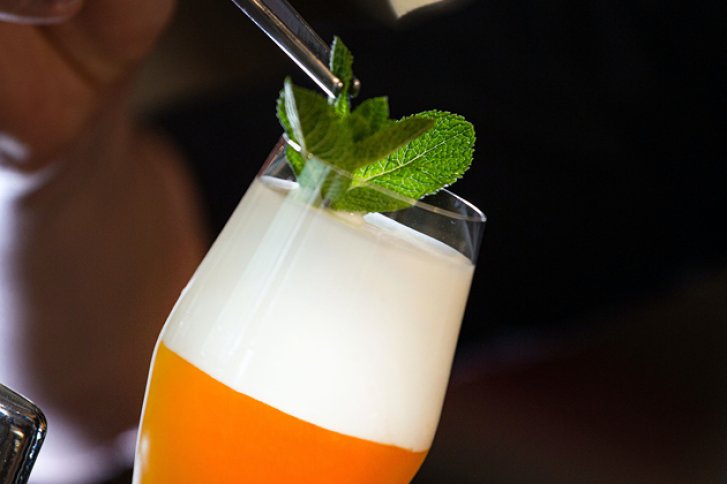 Ein Cocktailglas mit Schaum, garniert mit Minzblättern, in einer Hand gehalten.