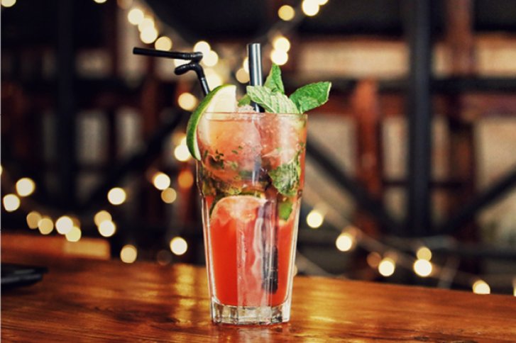 Ein Cocktailglas mit Strohhalm steht auf einem Holztisch, umgeben von Lichterkettenhintergrund.