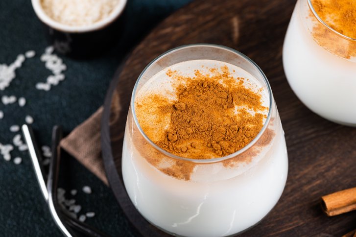 Ein Glas mit Milchgetränk, bestreut mit Zimt, steht auf einem dunklen Holztablett.