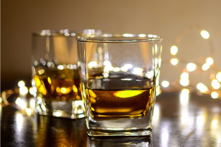 Zwei gefüllte Whiskygläser stehen auf einem Tisch, umgeben von unscharfen Lichterketten.