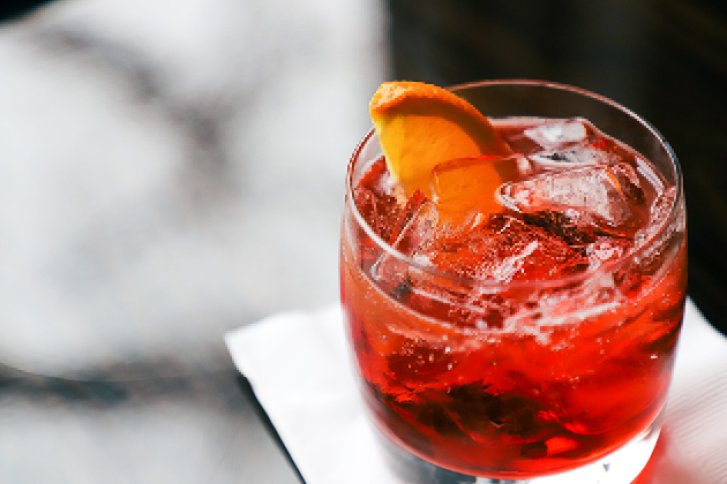 Ein Glas mit rotem Getränk und Eis auf weißer Serviette, dekoriert mit Orangenscheibe.