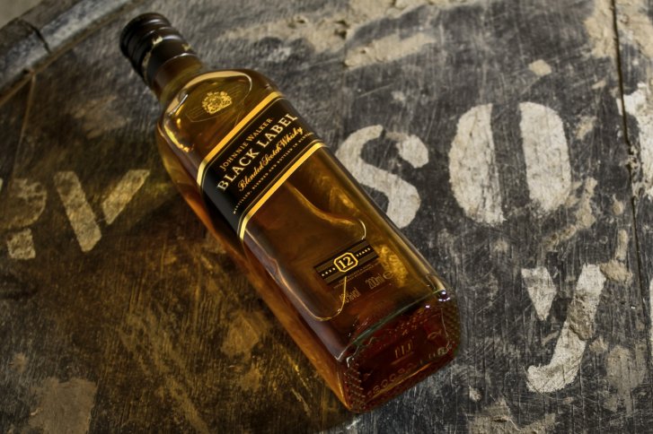 Eine Whiskyflasche liegt auf einem alten, beschrifteten Holztisch.