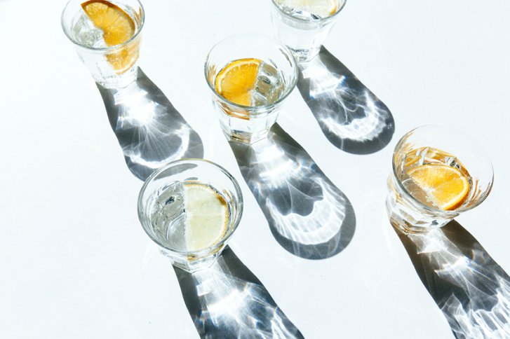 Gläser mit Orangenscheiben projizieren Schattenmuster auf eine weiße Oberfläche.