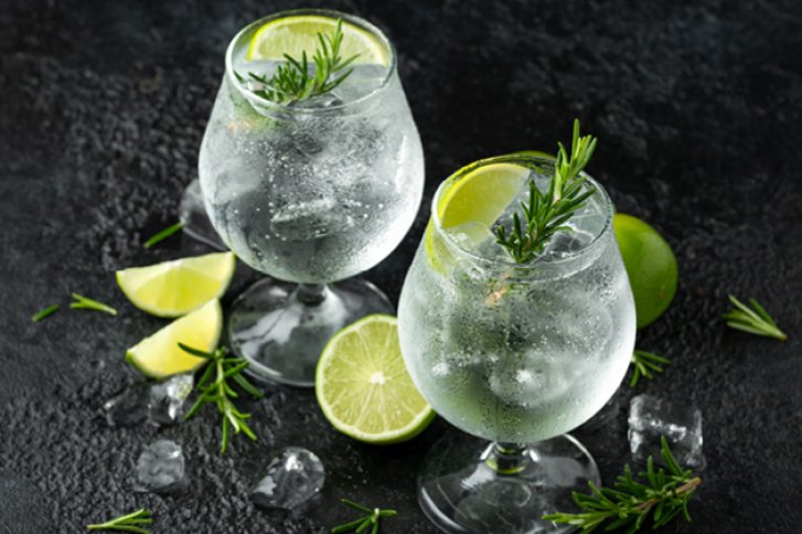 Zwei Gin-Tonic-Gläser mit Limettenscheiben und Rosmarin auf einem dunklen Hintergrund mit Eiswürfeln.