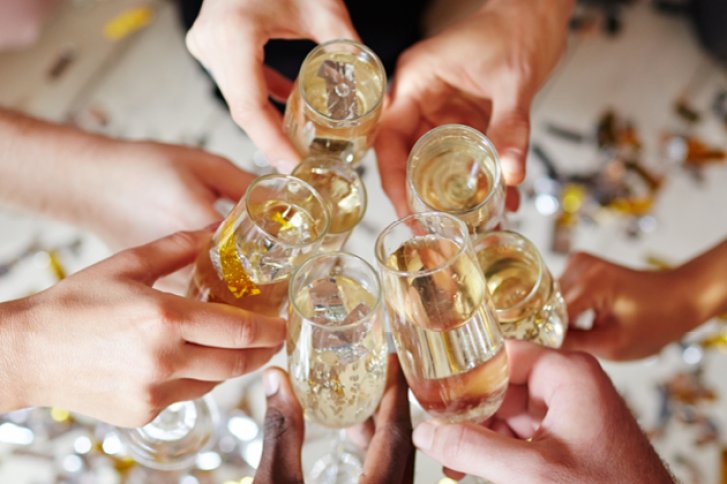 Gläser stoßen an, feiernde Hände, umgeben von verstreutem Konfetti auf einem hellen Untergrund.