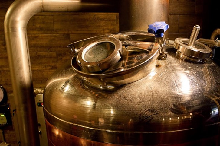 Metalltank still stehend, umgeben von Rohrleitungen, in einem industriellen Raum mit Holzwänden.