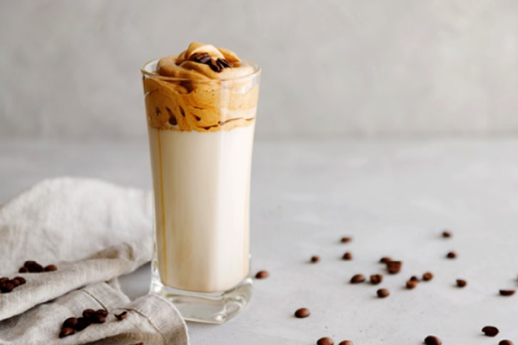 Ein Glas Dalgona-Kaffee steht auf einem Tisch, umgeben von Kaffeebohnen und einem Tuch.