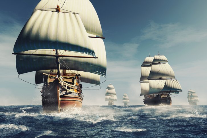 Mehrere Segelschiffe segeln auf hoher See bei klarem, leicht bewölktem Himmel.