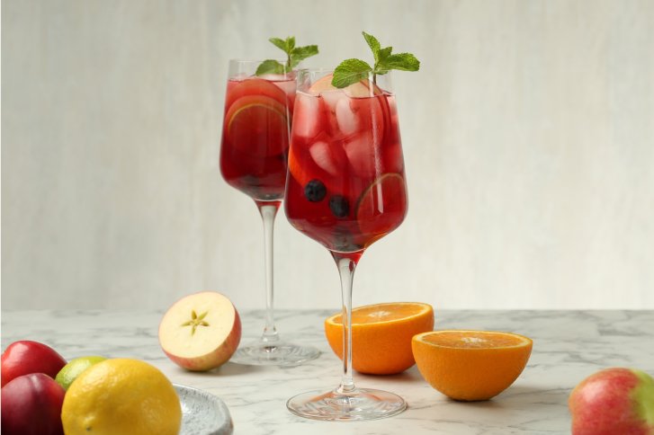 Zwei Weingläser mit rotem Getränk, Zitrusfrüchten und Minze stehen auf marmornem Tisch.