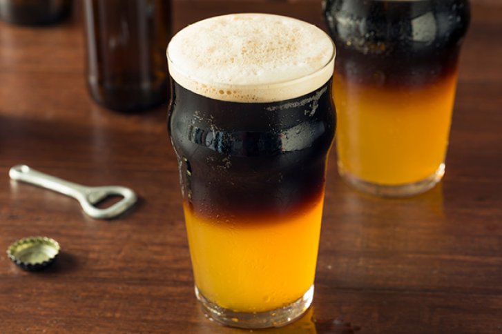 Bierglas steht auf Holztisch, halb dunkel, halb hell, daneben Flaschenöffner und Kronkorken.