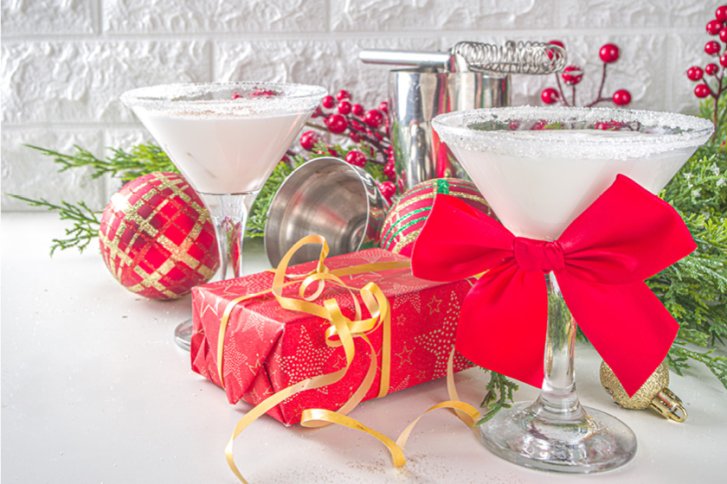 Zwei Cocktails stehen dekorativ mit roten Schleifen im weihnachtlichen Dekor mit Geschenken und Kugeln.