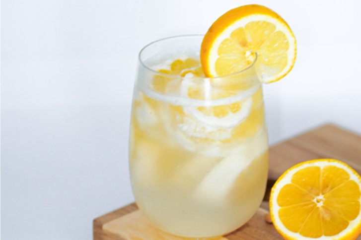 Ein Glas mit Zitronenscheiben und Eis, auf einem Holzbrett stehend.