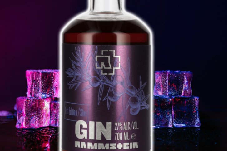 Eine Gin-Flasche steht vor bunten Eiswürfeln, dunkelvioletter Hintergrund, Etikett zeigt Kräuter.