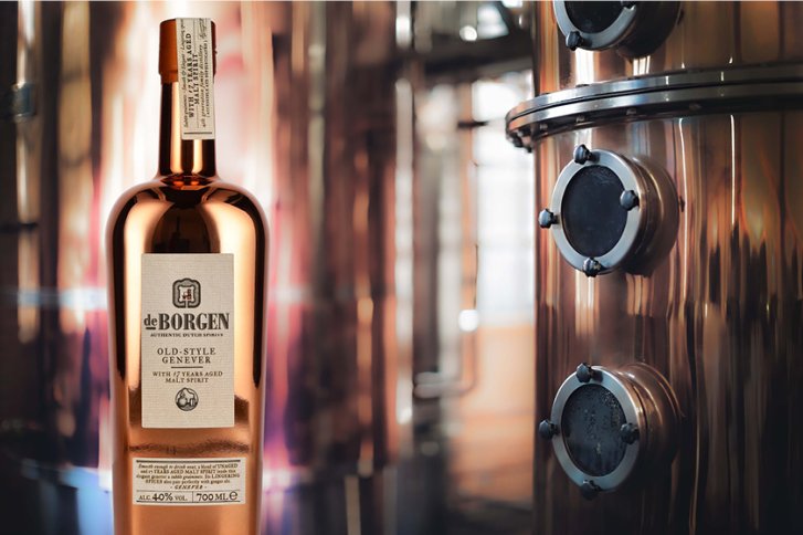 Kupferfarbene Gin-Flasche steht vor glänzender Brennerei-Ausrüstung in einem industriellen Umfeld.